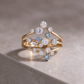 The Starpath Ring in 18K gold vermeil over sterling silver, with white moissanite and pale lab-created blue sapphires set along three sweeping gold arcs, resting on a light stone surface.