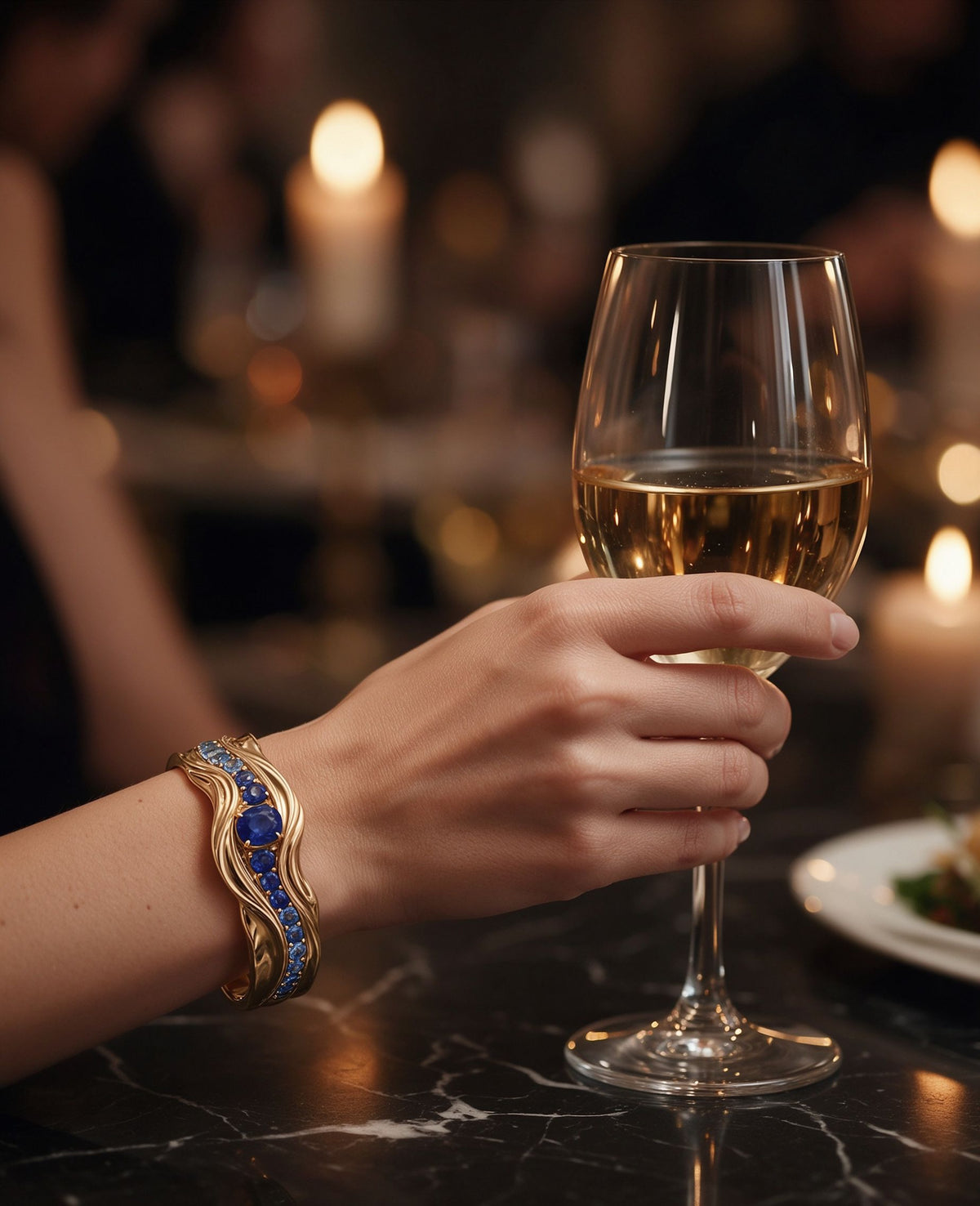 The Nereid Cuff worn at a candlelit dinner, the blue sapphire wave resting across the wrist beside a glass of wine, showing its true scale